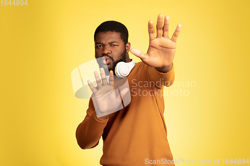 Image of Young african-american man\'s portrait isolated on yellow studio background, facial expression. Beautiful male half-lenght portrait with copyspace.