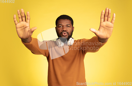 Image of Young african-american man\'s portrait isolated on yellow studio background, facial expression. Beautiful male half-lenght portrait with copyspace.