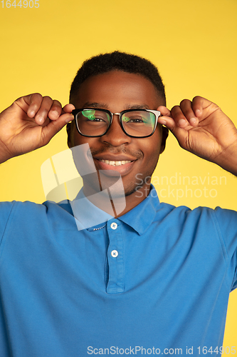 Image of Young african-american man\'s portrait isolated on yellow studio background, facial expression. Beautiful male half-lenght portrait with copyspace.