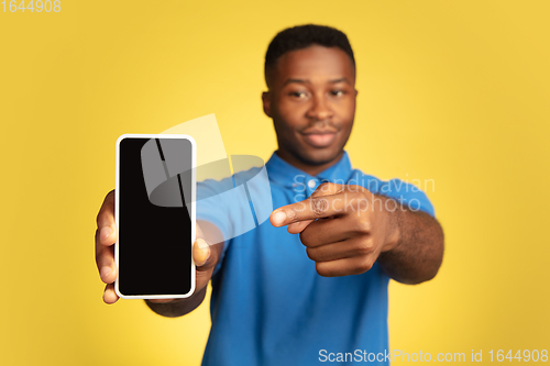 Image of Young african-american man\'s portrait isolated on yellow studio background, facial expression. Beautiful male half-lenght portrait with copyspace.