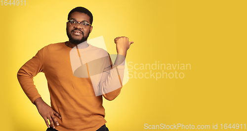 Image of Young african-american man\'s portrait isolated on yellow studio background, facial expression. Beautiful male half-lenght portrait with copyspace.