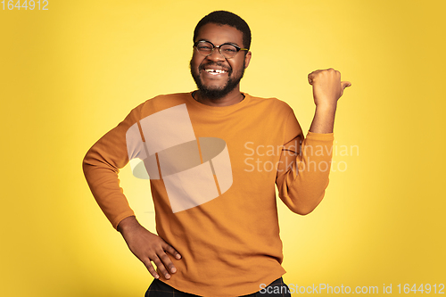 Image of Young african-american man\'s portrait isolated on yellow studio background, facial expression. Beautiful male half-lenght portrait with copyspace.