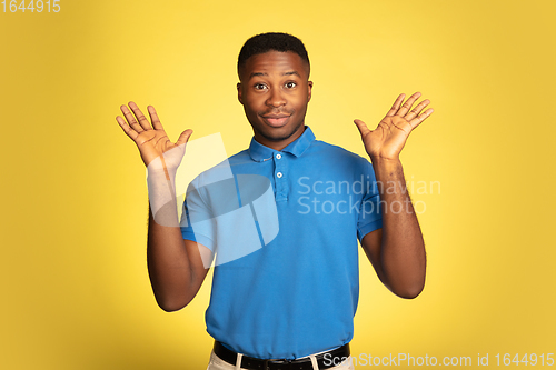 Image of Young african-american man\'s portrait isolated on yellow studio background, facial expression. Beautiful male half-lenght portrait with copyspace.