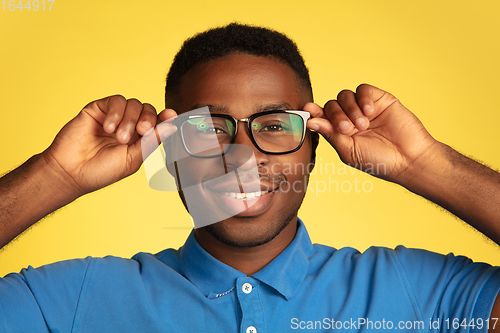 Image of Young african-american man\'s portrait isolated on yellow studio background, facial expression. Beautiful male half-lenght portrait with copyspace.