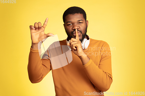 Image of Young african-american man\'s portrait isolated on yellow studio background, facial expression. Beautiful male half-lenght portrait with copyspace.