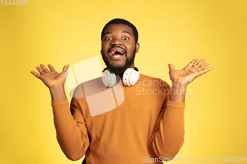 Image of Young african-american man\'s portrait isolated on yellow studio background, facial expression. Beautiful male half-lenght portrait with copyspace.