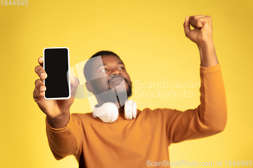 Image of Young african-american man\'s portrait isolated on yellow studio background, facial expression. Beautiful male half-lenght portrait with copyspace.