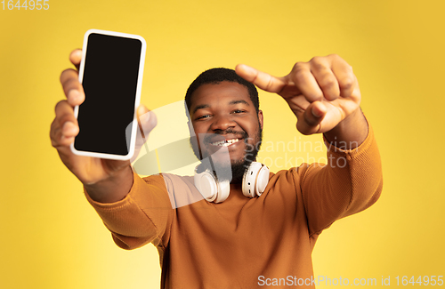 Image of Young african-american man\'s portrait isolated on yellow studio background, facial expression. Beautiful male half-lenght portrait with copyspace.