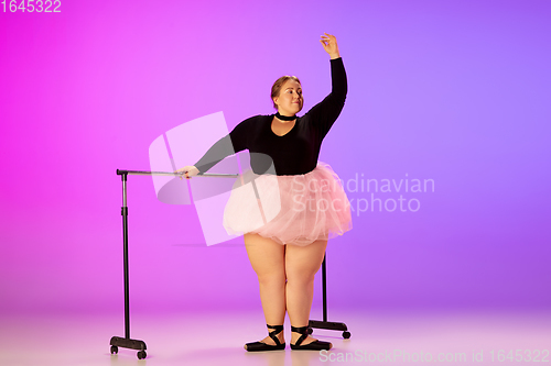 Image of Beautiful caucasian plus size model practicing ballet dance on gradient purple-pink studio background in neon light