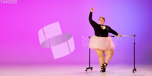 Image of Beautiful caucasian plus size model practicing ballet dance on gradient purple-pink studio background in neon light