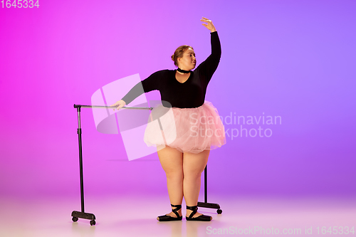 Image of Beautiful caucasian plus size model practicing ballet dance on gradient purple-pink studio background in neon light