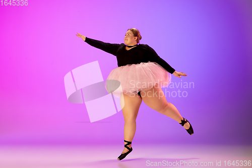 Image of Beautiful caucasian plus size model practicing ballet dance on gradient purple-pink studio background in neon light