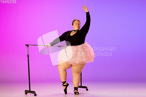 Image of Beautiful caucasian plus size model practicing ballet dance on gradient purple-pink studio background in neon light