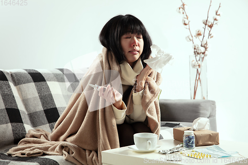 Image of Woman wrapped in a plaid looks sick, ill, sneezing and coughing sitting at home indoors