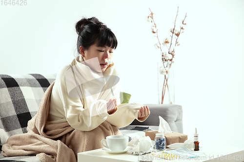 Image of Woman wrapped in a plaid looks sick, ill, sneezing and coughing sitting at home indoors