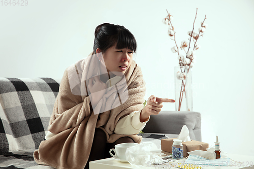 Image of Woman wrapped in a plaid looks sick, ill, sneezing and coughing sitting at home indoors