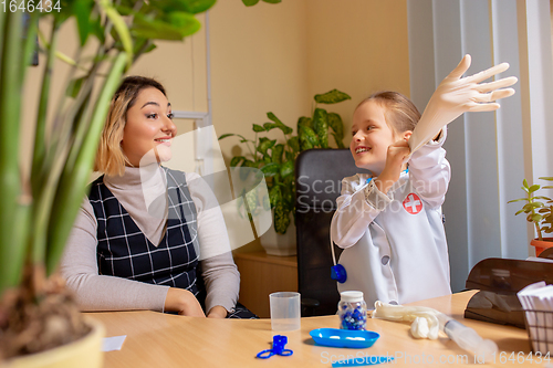 Image of Paediatrician doctor examining a child in comfortabe medical office. Little girl playing pretends like doctor for woman