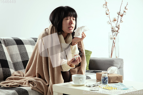 Image of Woman wrapped in a plaid looks sick, ill, sneezing and coughing sitting at home indoors