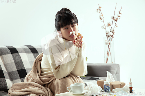 Image of Woman wrapped in a plaid looks sick, ill, sneezing and coughing sitting at home indoors