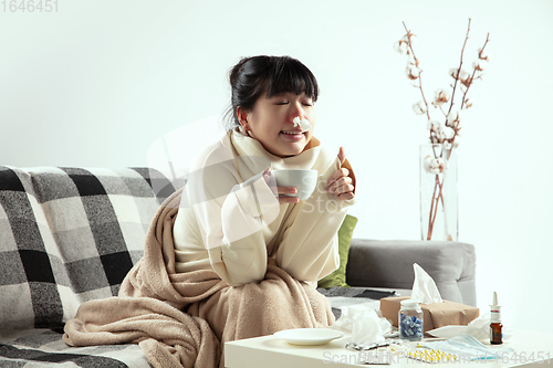 Image of Woman wrapped in a plaid looks sick, ill, sneezing and coughing sitting at home indoors