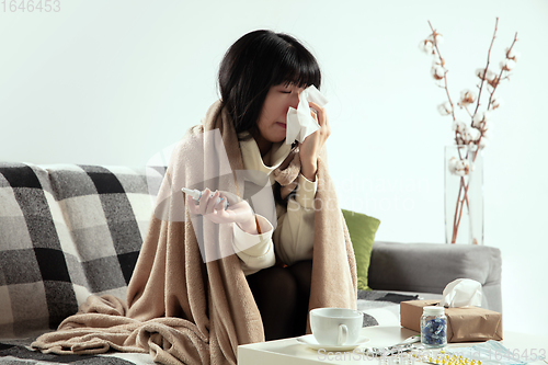 Image of Woman wrapped in a plaid looks sick, ill, sneezing and coughing sitting at home indoors