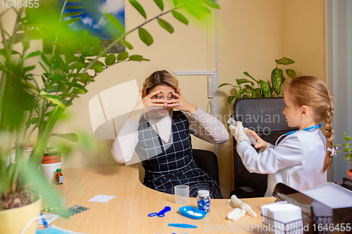 Image of Paediatrician doctor examining a child in comfortabe medical office. Little girl playing pretends like doctor for woman