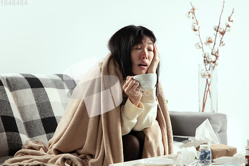 Image of Woman wrapped in a plaid looks sick, ill, sneezing and coughing sitting at home indoors