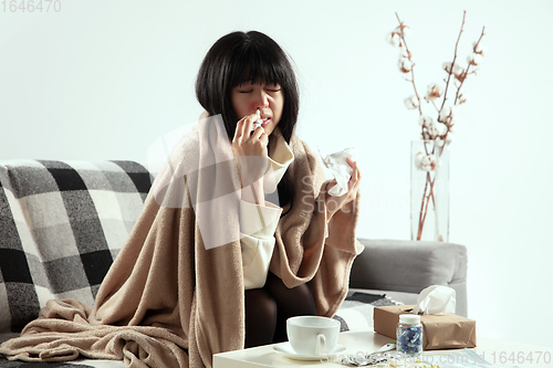 Image of Woman wrapped in a plaid looks sick, ill, sneezing and coughing sitting at home indoors