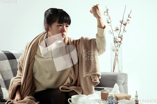 Image of Woman wrapped in a plaid looks sick, ill, sneezing and coughing sitting at home indoors