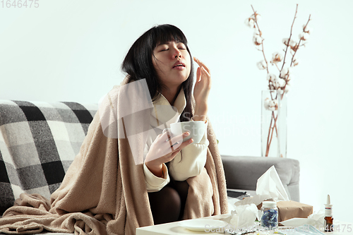 Image of Woman wrapped in a plaid looks sick, ill, sneezing and coughing sitting at home indoors