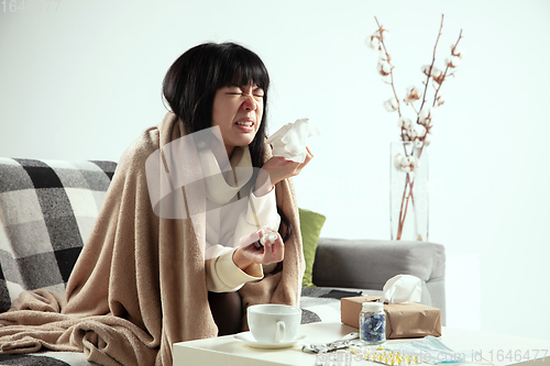 Image of Woman wrapped in a plaid looks sick, ill, sneezing and coughing sitting at home indoors