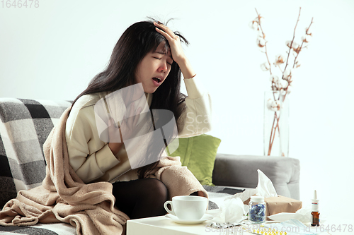 Image of Woman wrapped in a plaid looks sick, ill, sneezing and coughing sitting at home indoors