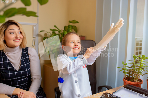 Image of Paediatrician doctor examining a child in comfortabe medical office. Little girl playing pretends like doctor for woman