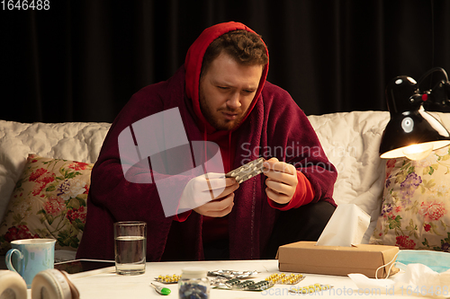 Image of Man wrapped in a plaid looks sick, ill, sneezing and coughing sitting at home indoors