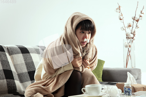 Image of Woman wrapped in a plaid looks sick, ill, sneezing and coughing sitting at home indoors