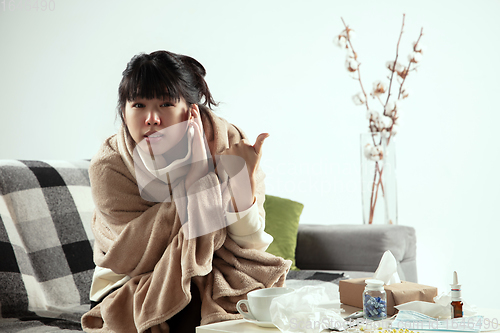 Image of Woman wrapped in a plaid looks sick, ill, sneezing and coughing sitting at home indoors