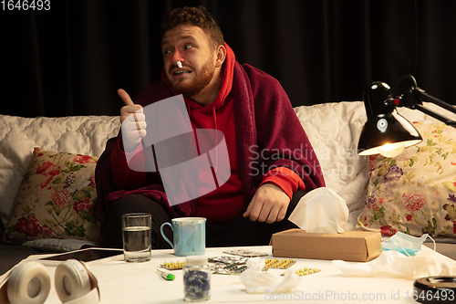 Image of Man wrapped in a plaid looks sick, ill, sneezing and coughing sitting at home indoors