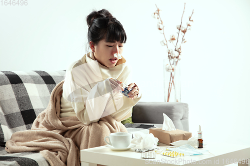 Image of Woman wrapped in a plaid looks sick, ill, sneezing and coughing sitting at home indoors