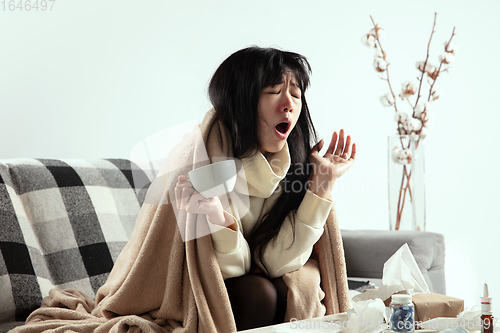 Image of Woman wrapped in a plaid looks sick, ill, sneezing and coughing sitting at home indoors