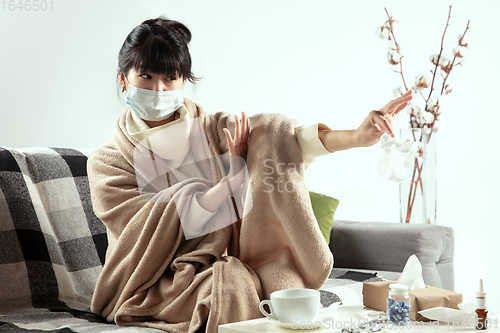 Image of Woman wrapped in a plaid and wearing face mask trying to protect herself from somebody\'s sick near by