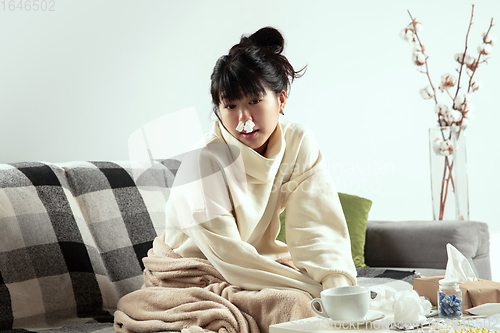 Image of Woman wrapped in a plaid looks sick, ill, sneezing and coughing sitting at home indoors