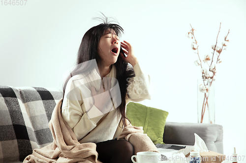 Image of Woman wrapped in a plaid looks sick, ill, sneezing and coughing sitting at home indoors