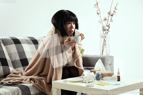 Image of Woman wrapped in a plaid looks sick, ill, sneezing and coughing sitting at home indoors