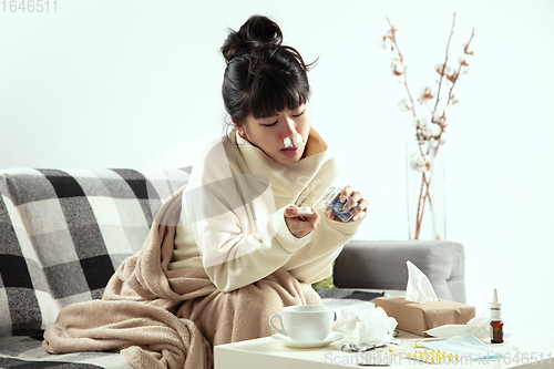 Image of Woman wrapped in a plaid looks sick, ill, sneezing and coughing sitting at home indoors