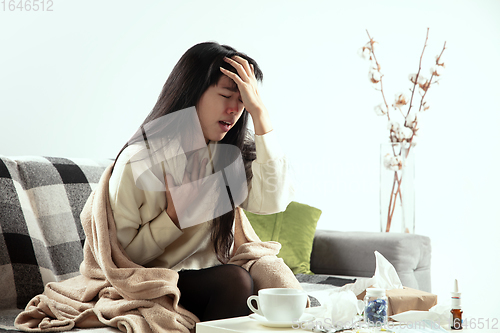 Image of Woman wrapped in a plaid looks sick, ill, sneezing and coughing sitting at home indoors