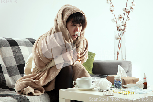 Image of Woman wrapped in a plaid looks sick, ill, sneezing and coughing sitting at home indoors