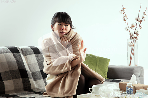 Image of Woman wrapped in a plaid looks sick, ill, sneezing and coughing sitting at home indoors