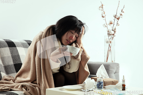 Image of Woman wrapped in a plaid looks sick, ill, sneezing and coughing sitting at home indoors