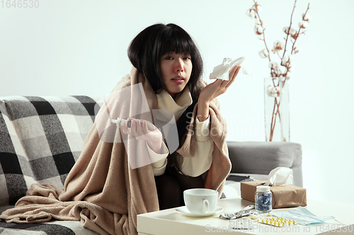 Image of Woman wrapped in a plaid looks sick, ill, sneezing and coughing sitting at home indoors