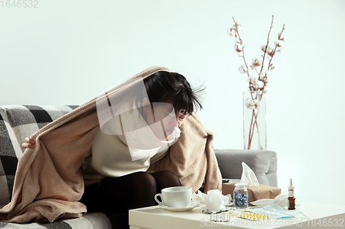 Image of Woman wrapped in a plaid looks sick, ill, sneezing and coughing sitting at home indoors